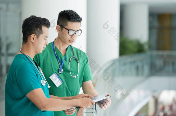 两名年轻的亚洲卫生专业人员站在<strong>医院</strong>的栏杆附近, 在剪贴板上讨论<strong>病历</strong>的侧视图