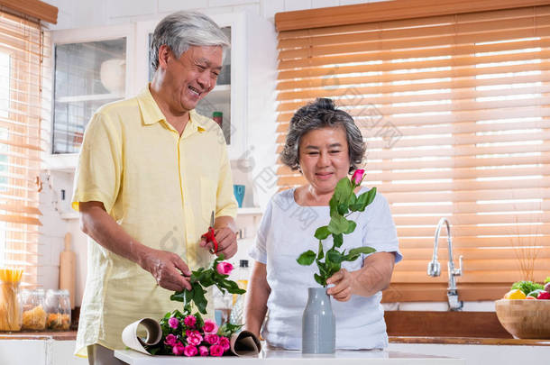 亚洲高级夫妇的丈夫和妻子的花<strong>安排</strong>花瓶在厨房的桌子在家里的情人节. 可爱的老夫妇的概念