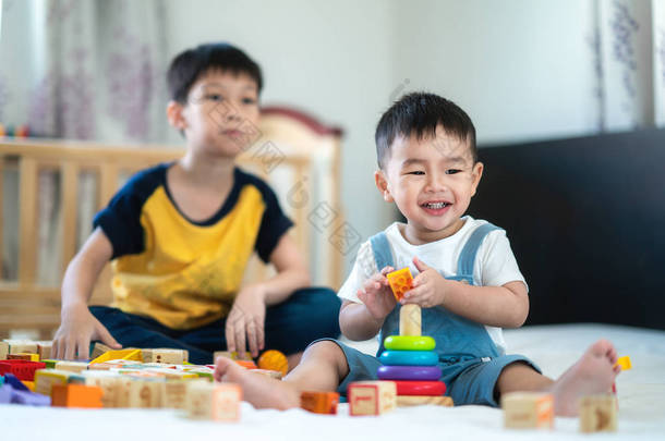 <strong>哥哥</strong>和一个微笑的男孩在床上玩玩具聚集, 这个模仿可以用于孩子, 家庭, 教育, 乐趣, 游戏, 家庭和玩具的概念