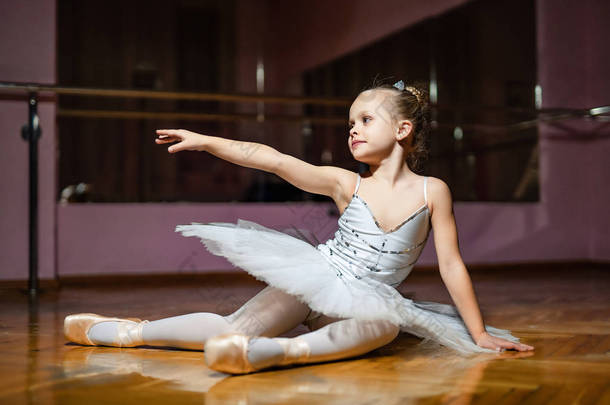 可爱的小芭蕾<strong>舞</strong>演员穿着白色的 tutu 坐在木地板上, 用右<strong>手指</strong>着芭蕾课。在演播室做运动的小<strong>舞</strong>者