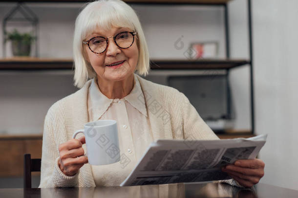 微笑的老年妇女坐在桌旁<strong>看报</strong>纸, 而在家里喝咖啡
