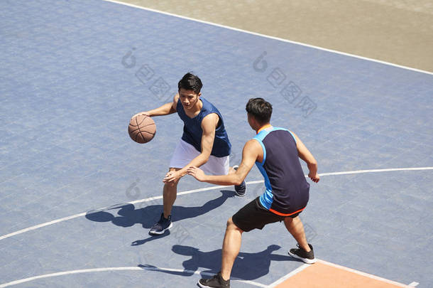 两个年轻的亚洲篮球运动员在户外赛场上一个打一个.