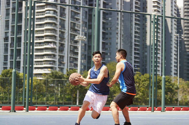 两个年轻的亚洲篮球运动员在户外<strong>赛场</strong>上一个打一个.
