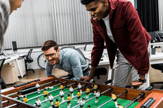 微笑的多元文化商人在办公室玩桌上足球