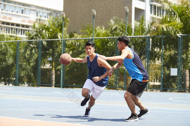 两个年轻的亚洲篮球运动员在户外赛场上一个打一个.