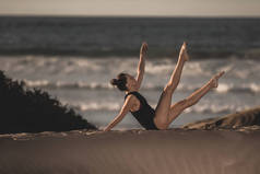 年轻优雅的女人坐在沙滩上, 在背景下与海景和平地做瑜伽体式