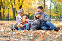 幸福的家庭坐在秋天城市公园在落叶。孩子们和家长摆姿势, 微笑, 玩耍和娱乐。明亮的黄色树.