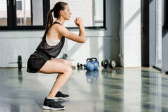 在健身工作室蹲着的坚定的女运动员的侧视图
