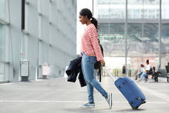 年轻黑人女子提着手提箱在机场行走的全长侧像