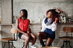 有吸引力的非洲裔美国人两个女孩的朋友坐在椅子上反对酒吧在酒吧.