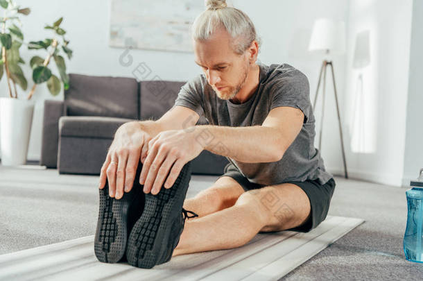 运动的成年人在运动服坐和伸展瑜伽垫在家里