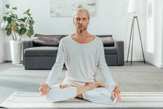 运动成年男子冥想在莲花位置上瑜伽垫在家里 