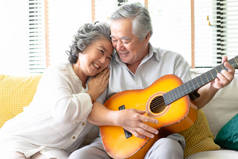 客厅里的情人。快乐的老年妇女抱着留胡子的男人在爱坐在沙发上, 而年轻的丈夫在客厅里弹吉他.