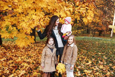 快乐的家庭在秋天散步。母亲和三女儿在公园散步, 享受美丽的秋天自然.