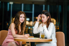 两个年轻和有吸引力的亚洲华人妇女坐在咖啡馆一起, 正在讨论一个记事本 