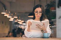 一个悲伤的美丽的女人看书在桌上与咖啡杯在咖啡馆