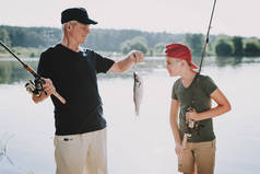 快乐爷爷和孙子在夏天在河上钓鱼。放松的户外。老人和男孩。湖边的人手里拿着钓鱼竿。夏天的运动。周末在河上。老年渔民.