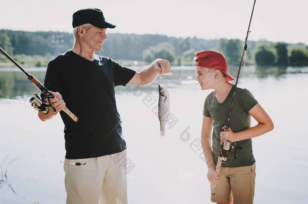 快乐爷爷和孙子在夏天在河上钓鱼。放松的户外。老人和男孩。湖边的人手里拿着钓鱼竿。夏天的运动。周末在河上。老年渔民.