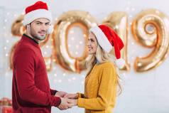 微笑的夫妇在圣诞老人手捧在家里与2019新年金色气球