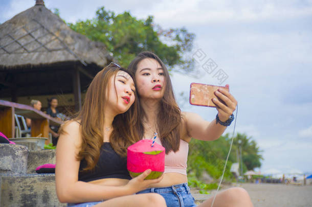 两个年轻快乐和有吸引力的亚洲华人和韩国妇女的生活方式肖像闲逛, 女朋友享受假日旅行在热带度假胜地带自拍图片与手机 