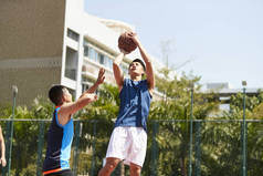 年轻的亚洲篮球运动员跳投, 而对手打防守试图阻止球.
