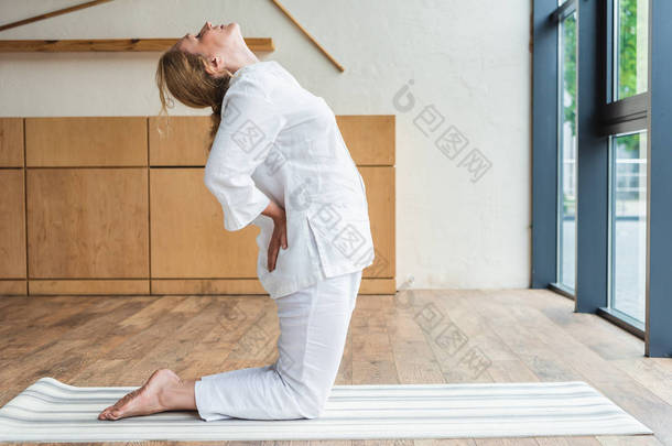 运动成熟妇女的侧面在瑜伽垫上练习瑜伽