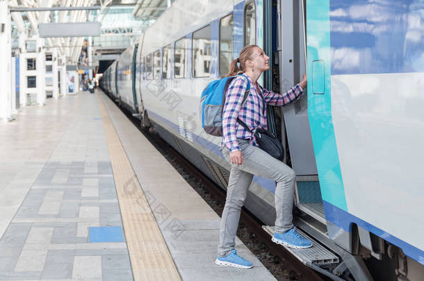 年轻的女<strong>游客</strong>进入火车。在<strong>火车站</strong>带着蓝色背包的漂亮女人。铁路旅行。现代高速列车.