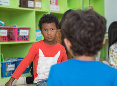 美国黑人男孩在幼儿园的学校图书馆里生气地看着朋友. 儿童教育理念