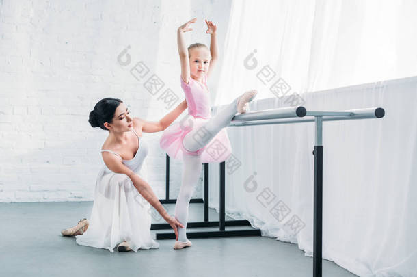 可爱的孩子在粉红色的芭蕾舞短裙伸展和看着相机, 而实践芭蕾与教师