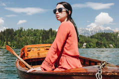 美丽的年轻妇女在太阳镜坐小船在风景秀丽的山湖, 流血, 斯洛文尼亚