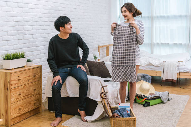 快乐的亚洲情侣选择在现代家居、情侣、生活方式和旅行者概念的客厅里准备旅行的衣服,