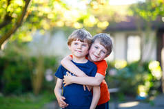 两个小小的活动学校的孩子男孩，双胞胎和兄弟姐妹拥抱在夏季的一天
