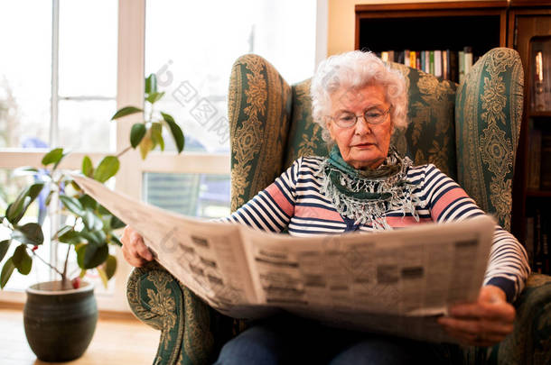 老年妇女在<strong>养老保险</strong>在家放松在读书报纸