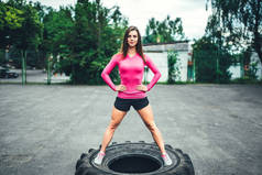 年轻的运动女孩锻炼室外与大轮胎