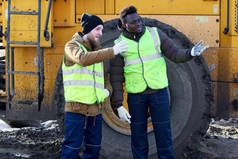 两名工人的肖像, 一个非洲裔美国人, 站在污垢旁边的重型工业转储卡车现场