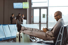微笑的生意人在机场大厅等待飞行时使用智能手机