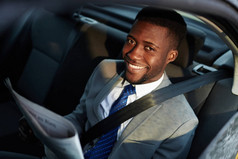 非洲裔美国商人坐在车后座上, 看着镜头, 在阳光的照射下, 乐呵呵地微笑着看报。