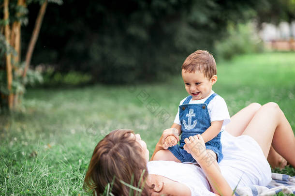 母亲和年轻的儿子玩在草地上。幸福的家庭在公园散步。妈妈和年幼的儿子吃水果。野餐。夏季.