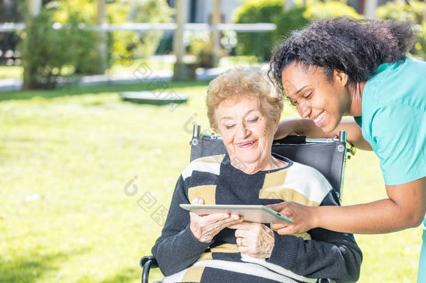 老妇在花园里帮助由护士使用平板电脑