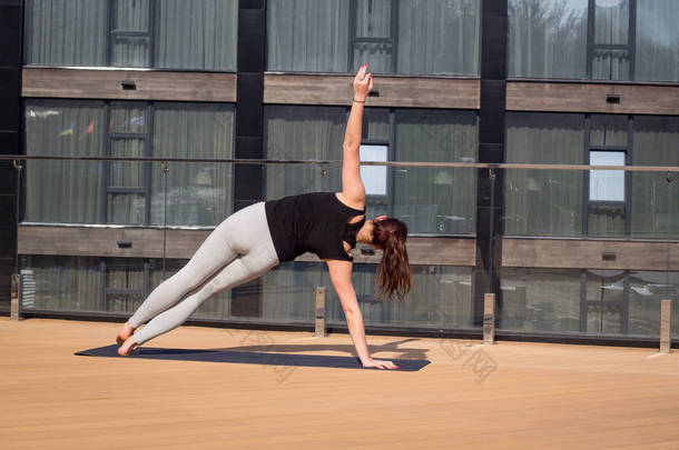 体育女人做伸展<strong>瑜伽</strong>运动酒店屋顶上的木地板在<strong>瑜伽垫</strong>上的立场