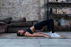 运动女孩做髋关节加薪或屁股电梯自由体操躺在她的阁楼公寓楼
