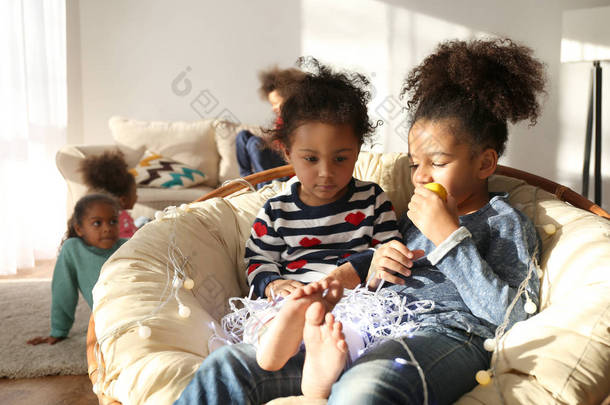 两个可爱的非洲女孩坐在扶手椅与柠檬和花环在家里