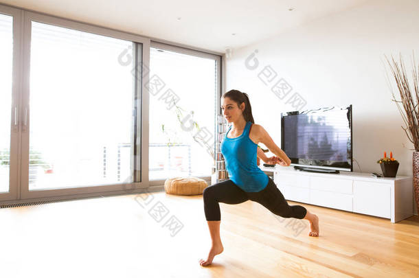 年轻的女人在家里做运动，拉伸<strong>胳膊</strong>和腿.