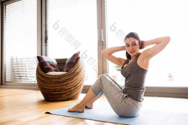 年轻的女人在家里做运动、 做仰卧起坐.