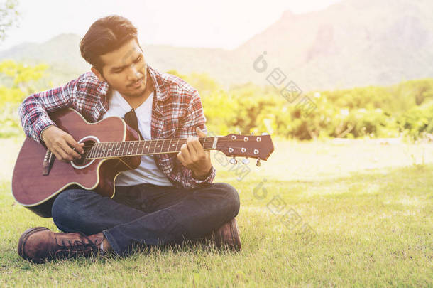英俊的男人在绿色草地上弹吉他