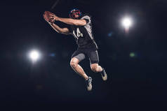 美国足球运动员的下视灯下的球跳跃在黑色的聚光灯下