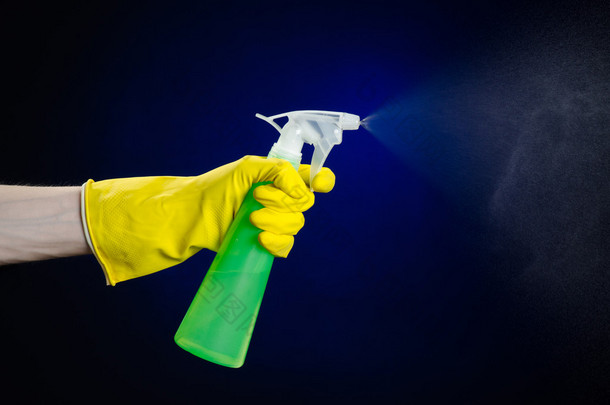 清洁的房子和更清洁的主题: 人的手中持有绿色喷雾瓶清洗暗蓝色背景上的黄色手套