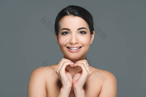 美丽的微笑的妇女与白色的牙齿显示心脏标志与双手隔绝灰色的肖像