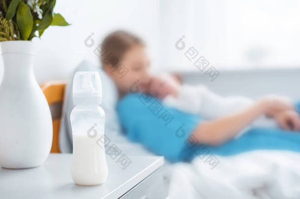 婴儿奶瓶与牛奶的特写镜头, 花瓶和母亲与新生婴儿躺在病床后面