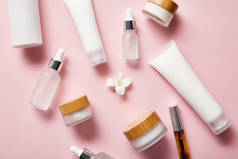 不同分散的化妆品容器和茉莉花在粉红色的中间的顶视图 